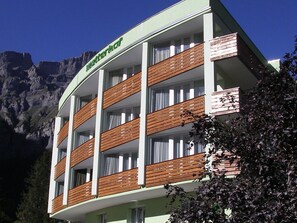 Ein mehrstöckiges Hotel mit Balkonen, einem Berg im Hintergrund und einem Schild, das es als Hotel kennzeichnet.