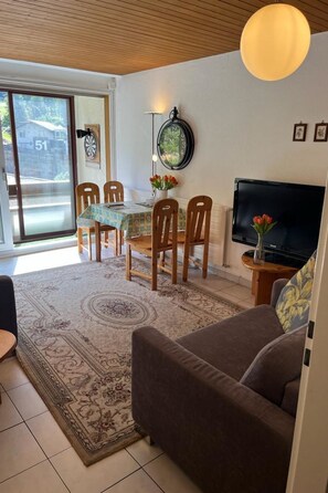 A living room with a sofa, a TV, a dining table with chairs, a wall clock, and a dartboard. - Fortuna 403 # 4-bed apartment, Dusche, WC 4-Bettwohnung, Dusche, WC by Interhome (Leukerbad)