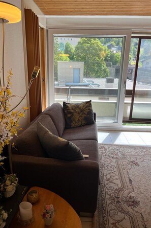 A modern living room with a sofa, a lamp, a vase with flowers, and a view of the outside. - Fortuna 403 # 4-bed apartment, Dusche, WC 4-Bettwohnung, Dusche, WC by Interhome (Leukerbad)