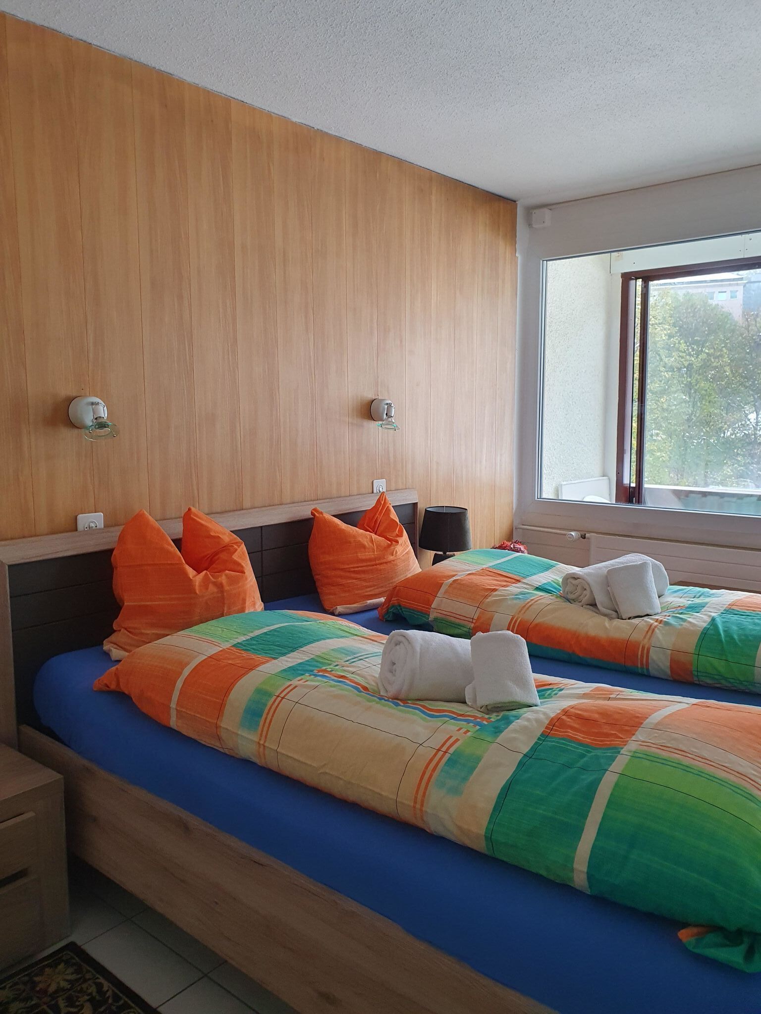 Ein Hotelzimmer mit zwei Betten, Holz-Kopfteilen und einem großen Fenster.