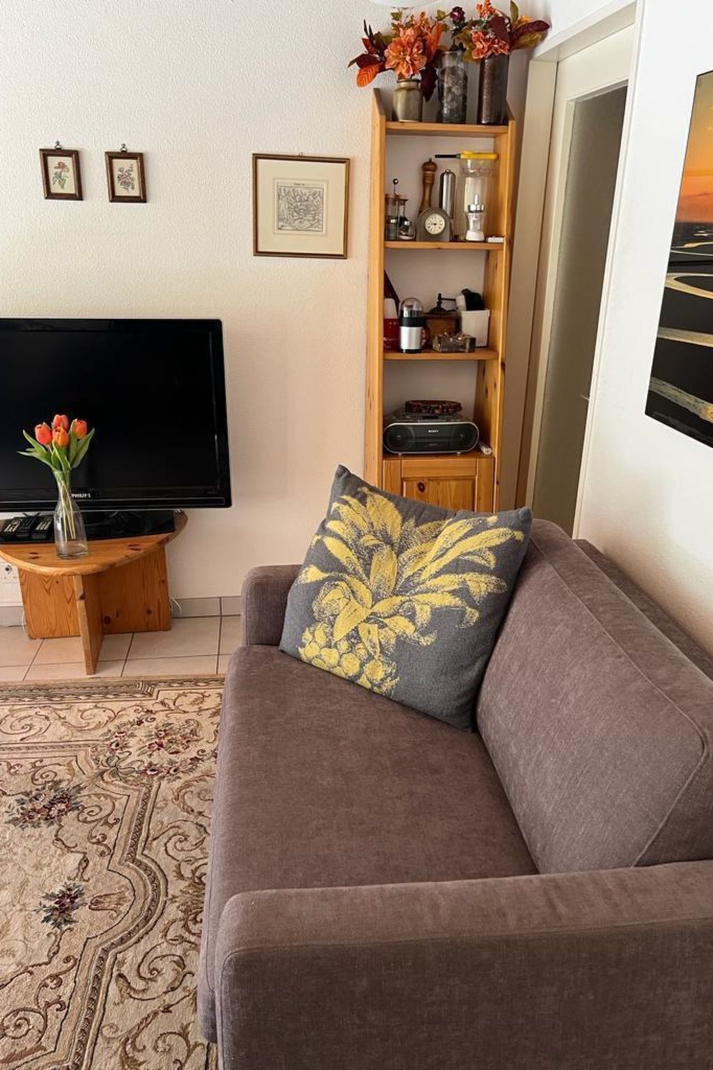 A living room with a sofa, a coffee table, a flat-screen TV, a bookshelf, and a decorative vase with flowers.