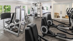 Une salle de sport équipée de divers appareils d’exercice, notamment des tapis de course et des appareils de musculation, avec de grandes fenêtres donnant sur un espace verdoyant.