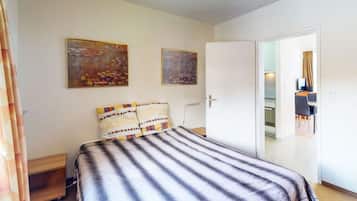 Ett hotellrum med en säng, två tavlor på väggen, en dörr som leder till ett kök och en gardin som syns delvis.