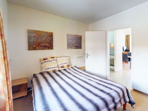 Ett hotellrum med en säng, två tavlor på väggen, en dörr som leder till ett kök och en gardin som syns delvis.