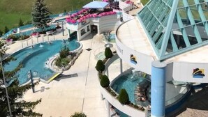 Un resort con una gran piscina, montañas al fondo y un edificio distintivo en azul y blanco.