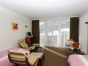 Habitación de hotel con dos camas, un escritorio, una silla, televisión y vistas a un paisaje nevado a través de las ventanas.