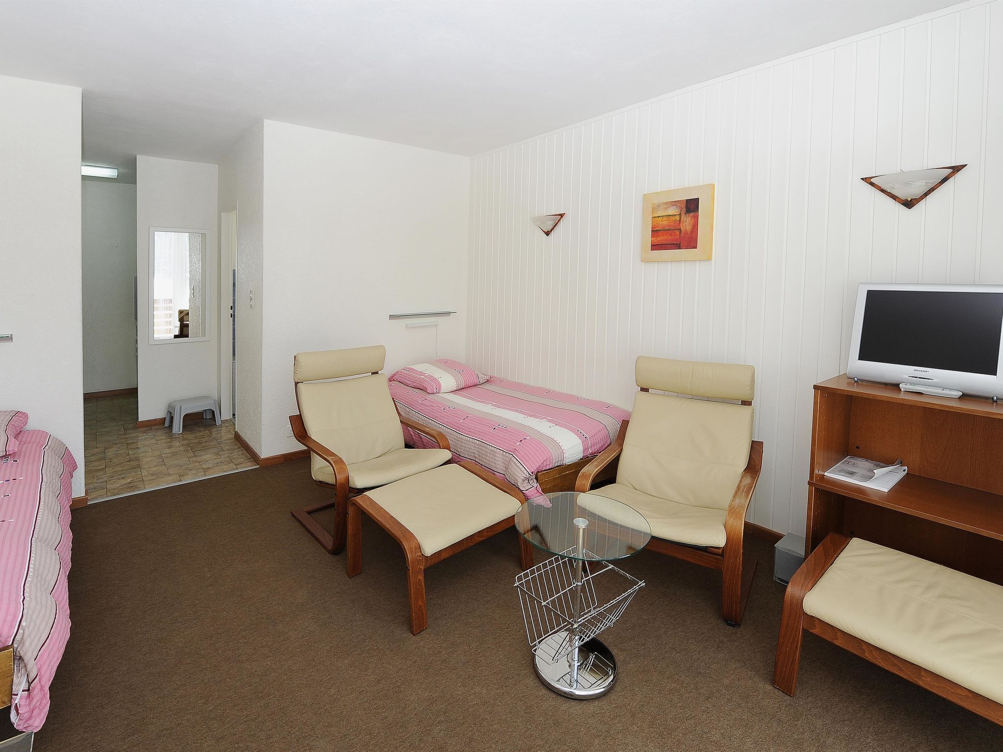 A room with a bed, two chairs, a small table, a television, and a picture on the wall.