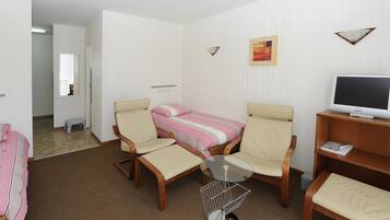 A room with a bed, two chairs, a small table, a television, and a picture on the wall.