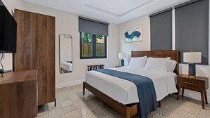 Habitación de hotel con cama, mesitas de noche, un espejo, una ventana y una obra de arte colgada en la pared.