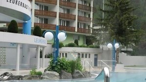 Een hotel met een zwembad, een bord waarop 'Leukerbad' staat en een bergachtige achtergrond.