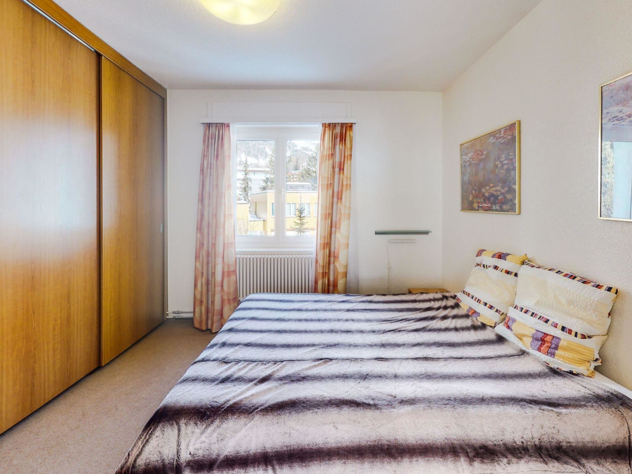 Um quarto com uma cama, um guarda-roupa, um radiador e uma janela com cortinas.