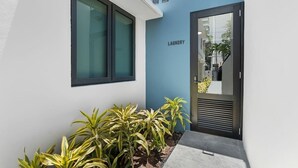 A modern building with a blue facade, a door labeled 'LAUNDRY,' and potted plants in front. - Cozy Miramar Studio | Queen Bed + WorkSpace (San Juan)