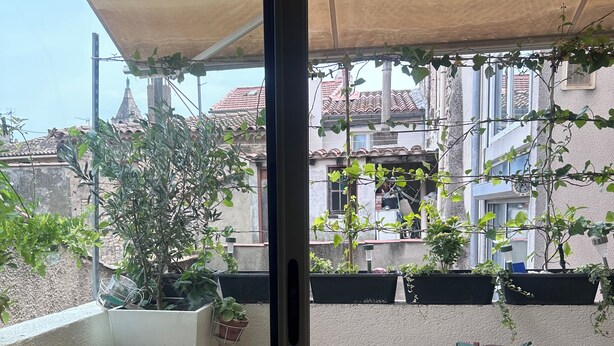 Ein Balkon mit zwei gepolsterten Stühlen, einem kleinen Tisch und Topfpflanzen.