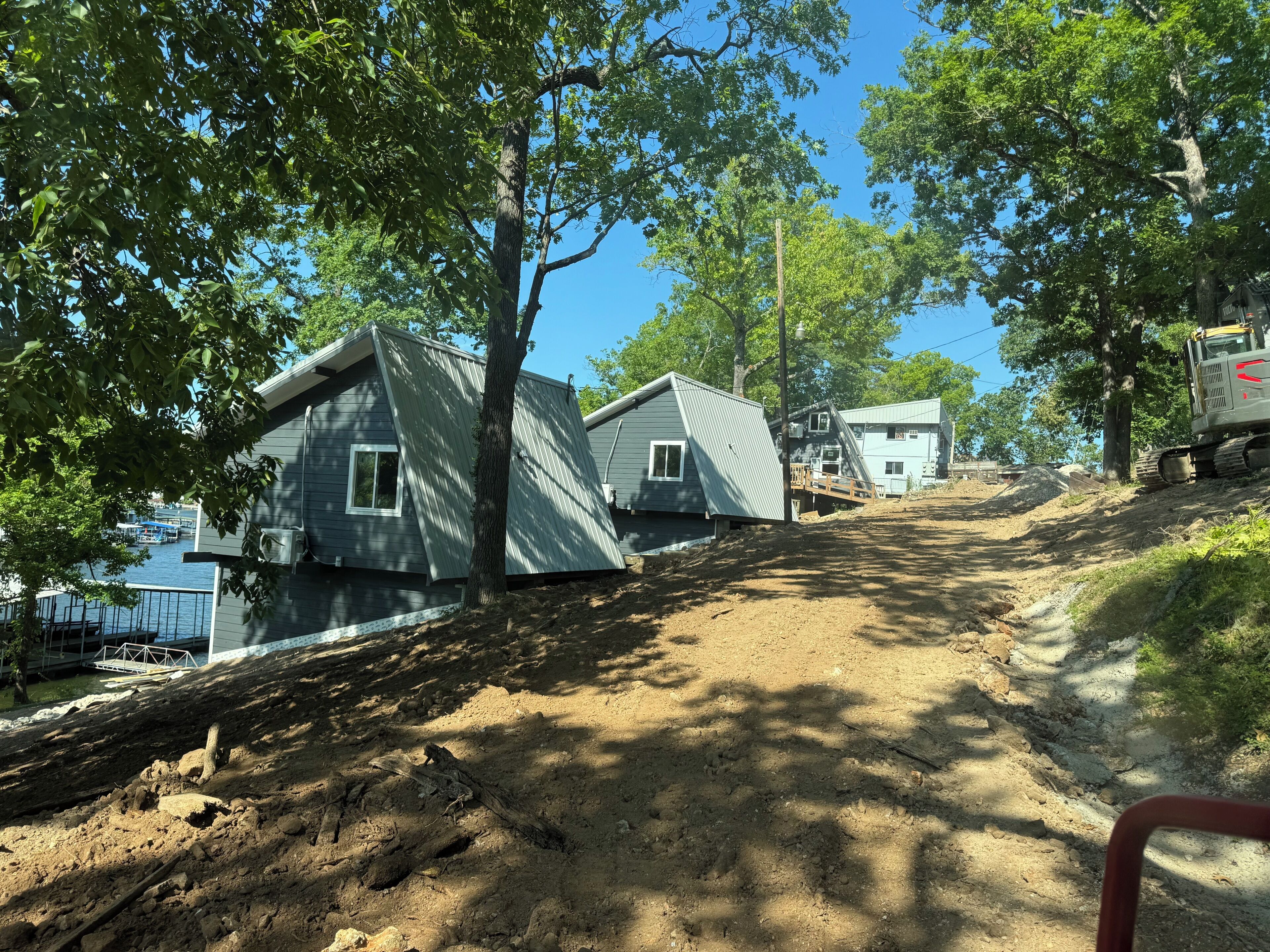 A residential area with houses on a hillside, a dirt path, and a construction vehicle.