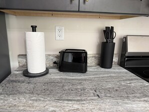 A kitchen counter with a paper towel holder, a toaster, and a utensil holder. - Cozy 840 sq ft A-frame cabin at North Shore Resort with lake views, 1 bedroom + loft (sleeps 6), full kitchen, island seating, and a private deck—perfect for relaxing getaways at Lake of the Ozarks. (Eldon)