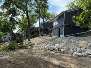 A construction site with a building under construction, a dirt path, and a large excavator. - Cozy 840 sq ft A-frame cabin at North Shore Resort with lake views, 1 bedroom + loft (sleeps 6), full kitchen, island seating, and a private deck—perfect for relaxing getaways at Lake of the Ozarks. (Eldon)
