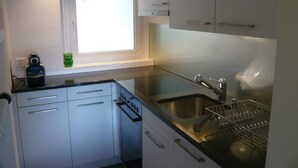 Una cocina compacta con ventana, horno empotrado, fregadero y escurreplatos.