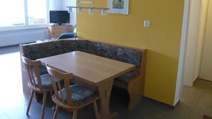 Un comedor con una mesa y sillas de madera, un banco y un televisor al fondo.