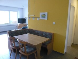 Ein Essbereich mit Holztisch und Stühlen, einer Bank und einem Fernseher im Hintergrund.