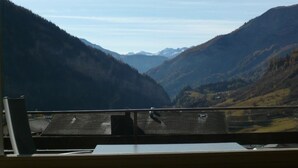 Un paisaje montañoso visto desde una ventana, con una mesa y sillas de madera en primer plano.