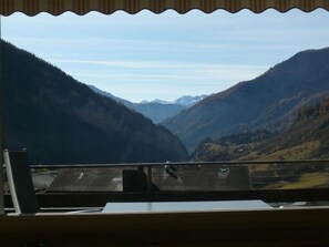 Eine Berglandschaft, die durch ein Fenster sichtbar ist, mit einem Holztisch und Stühlen im Vordergrund.