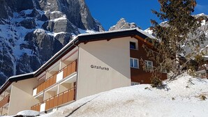 Un edificio con el nombre 'Gitzifurka' en su fachada, rodeado de montañas nevadas y un cielo azul despejado.