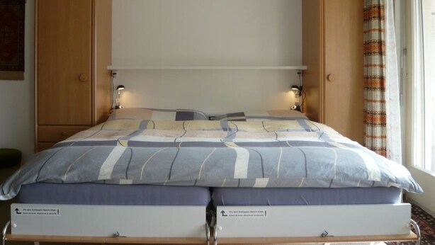 Una cama con cabecera, dos mesitas de noche y una ventana con cortinas.