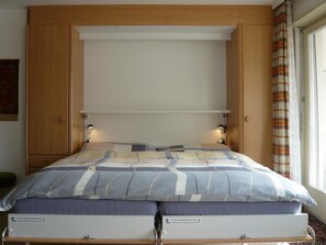 A bed with a headboard, two bedside tables, and a window with curtains. - Gitzifurka 4 # 4-bed apartment, Dusche, WC 4-Bettwohnung, Dusche, WC by Interhome (Leukerbad)