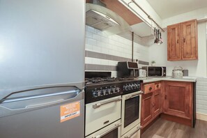 A kitchen with a stove, microwave, oven, and wooden cabinets. - Shoreline Apartment No.3 (Newquay)
