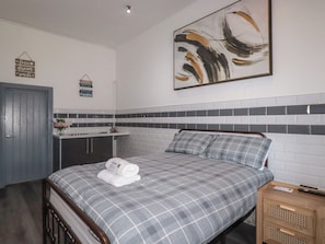A hotel room with a bed, a nightstand, a bathroom with a sink, and a towel on the bed. - Shoreline Apartment No.3 (Newquay)
