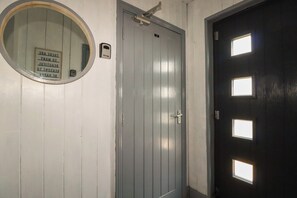 A room with a grey door, a round mirror, and a small sign with text. - Shoreline Apartment No.3 (Newquay)