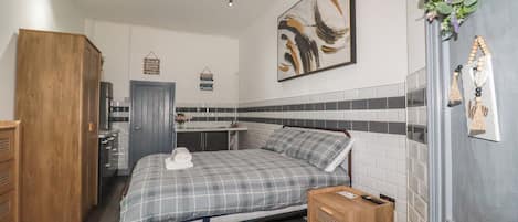 A bedroom with a bed, a wooden wardrobe, a bedside table, a wall-mounted artwork, and a small plant.