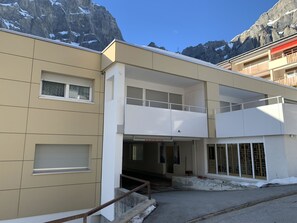 A multi-story building with a flat facade, large windows, and a staircase leading to the entrance. - Salute 206 # 4-bed apartment, Dusche, WC 4-Bettwohnung, Dusche, WC by Interhome (Leukerbad)