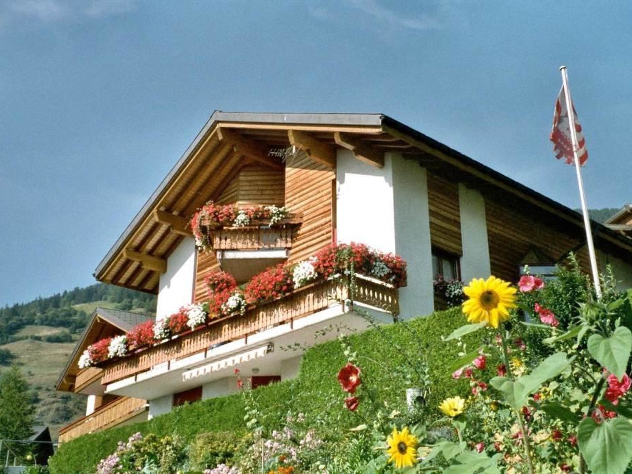 A chalet with wooden balconies, a flag, and a hillside view.