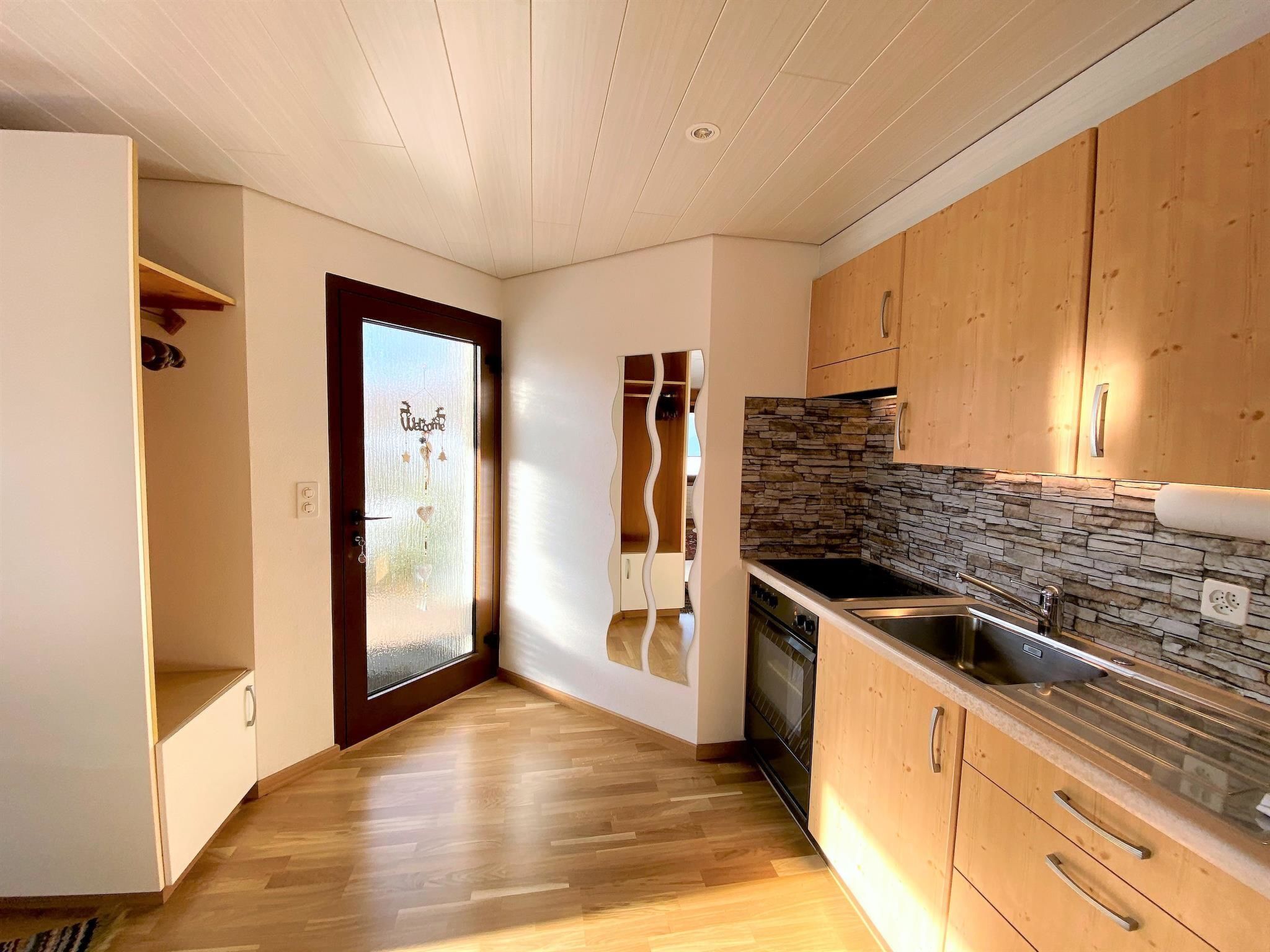 A modern kitchen with wooden cabinets, a stone backsplash, and a built-in oven.