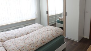 A bedroom with a bed, a wardrobe, a radiator, and a window with curtains. - Europe 16 # 4-bed apartment, Bad, WC 4-bed apartment, Bad, WC by Interhome (Leukerbad)
