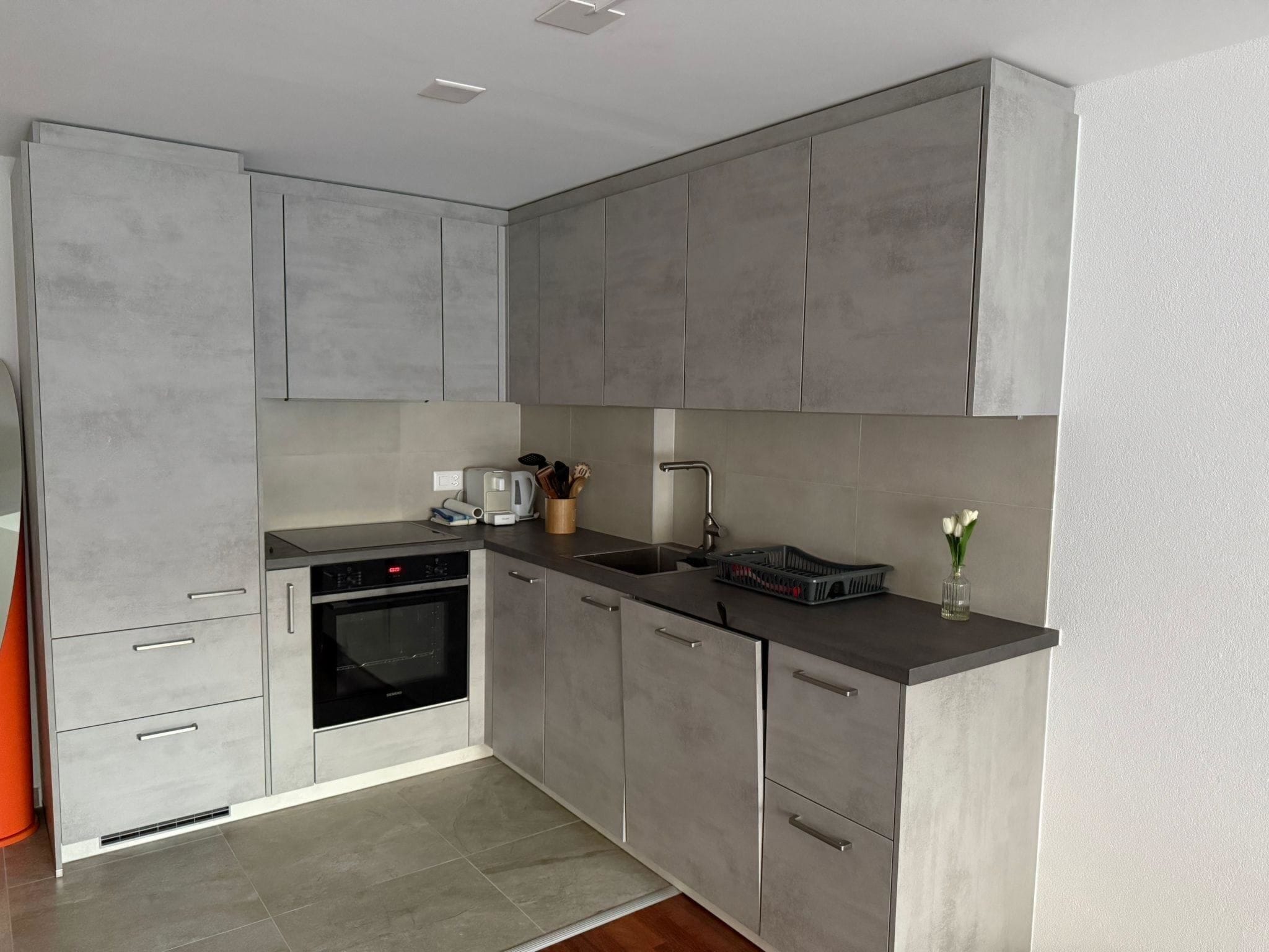 Eine moderne Küche mit grauen Schränken, einem eingebauten Backofen, einer Spüle und einer Arbeitsplatte mit verschiedenen Gegenständen.