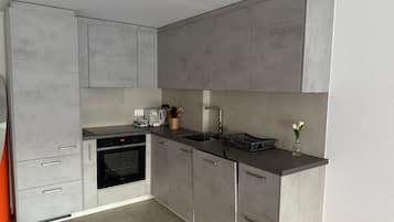 Eine moderne Küche mit grauen Schränken, einem eingebauten Backofen, einer Spüle und einer Arbeitsplatte mit verschiedenen Gegenständen.