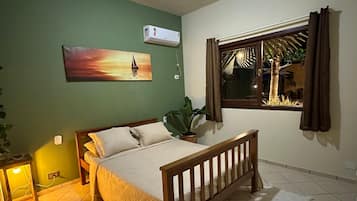 Une chambre à coucher avec un lit, une fenêtre avec des rideaux, un climatiseur fixé au mur et un tableau.
