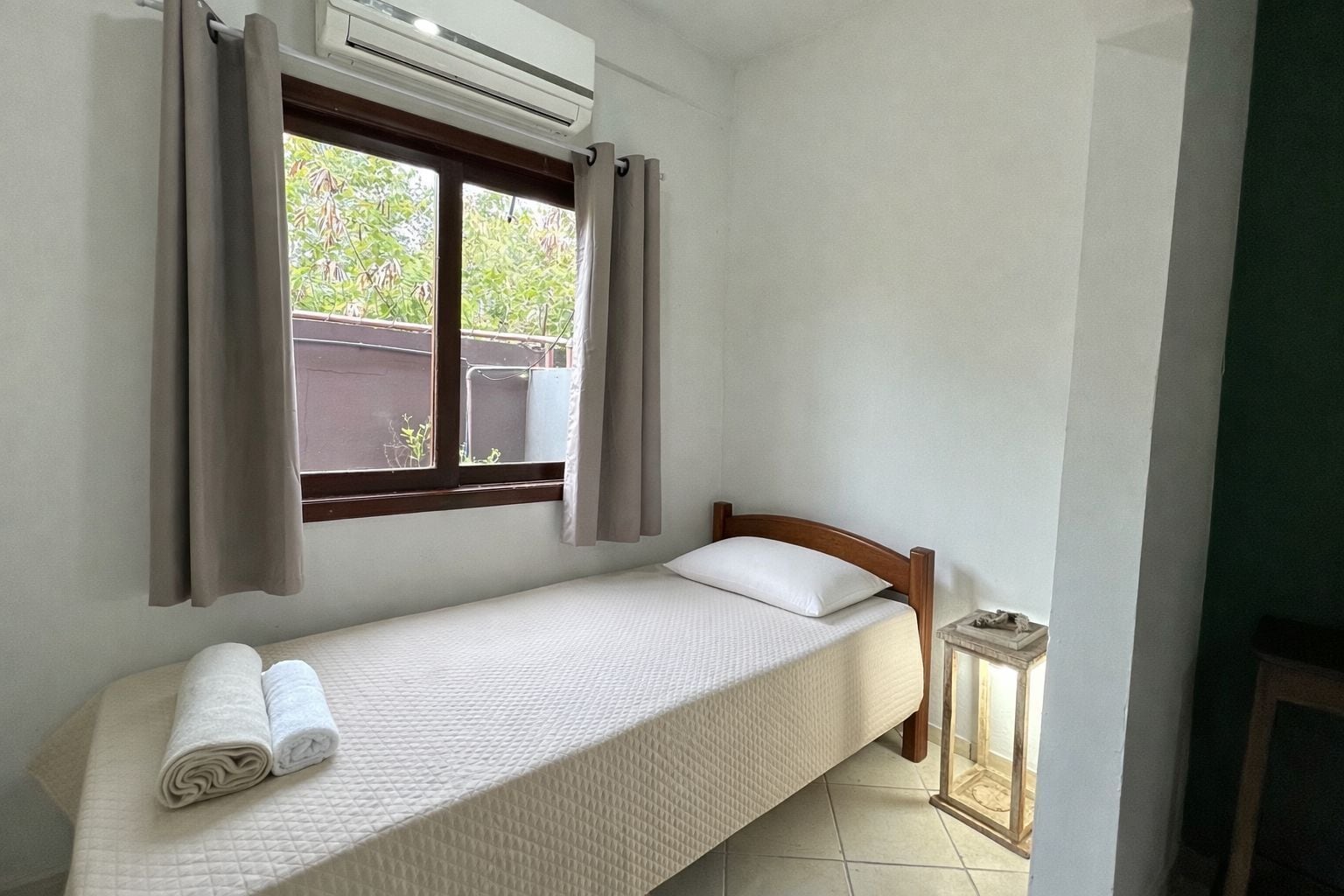 Uma cama de casal com cabeceira de madeira, uma janela com cortinas e um aparelho de ar condicionado acima.