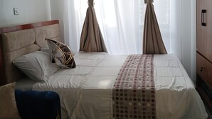 Quarto de hotel com cama, uma cadeira azul, guarda-roupa de madeira e uma mesa redonda.