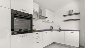 A modern kitchen with white cabinetry, a black oven, stainless steel shelves, and a built-in stove. - Cozy house with jaccuzzi and barbecue (Dobreć)