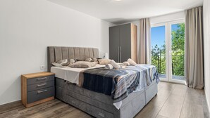 A bedroom with a bed, a wardrobe, a bedside table, and a view of greenery through a sliding door. - Cozy house with jaccuzzi and barbecue (Dobreć)