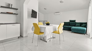 A modern kitchen with white cabinets, a dining table with yellow chairs, and a green sofa in a bright living area. - Cozy house with jaccuzzi and barbecue (Dobreć)