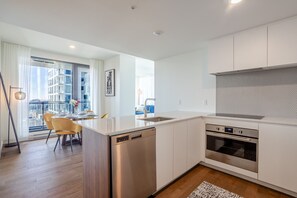 A modern kitchen with a dishwasher, oven, and a dining area with chairs and a table. - The Azure Rise | 2B1B Condo in Downtown MTL (Montreal)