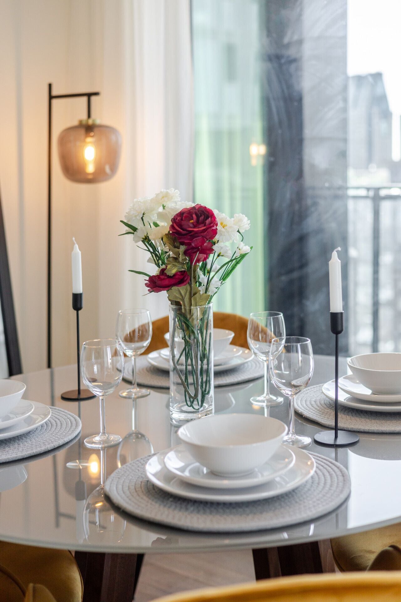 A dining table set with white plates, clear glasses, and a vase with flowers.