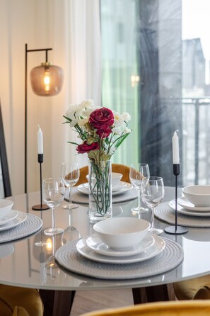 A dining table set with white plates, clear glasses, and a vase with flowers. - The Azure Rise | 2B1B Condo in Downtown MTL (Montreal)