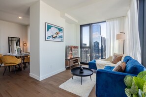 A modern living room with a sofa, a coffee table, a TV, and a dining area with chairs and a table. - The Azure Rise | 2B1B Condo in Downtown MTL (Montreal)