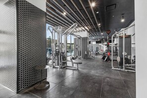 A gym with various exercise equipment, a hexagonal patterned wall, and a large window providing natural light. - The Azure Rise | 2B1B Condo in Downtown MTL (Montreal)