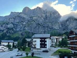 A mountain village with modern buildings, a parking area, and a prominent rocky mountain backdrop. - Floralp 5 # 4-bed apartment, Bad, WC 4-Bettwohnung, Bad, WC by Interhome (Leukerbad)